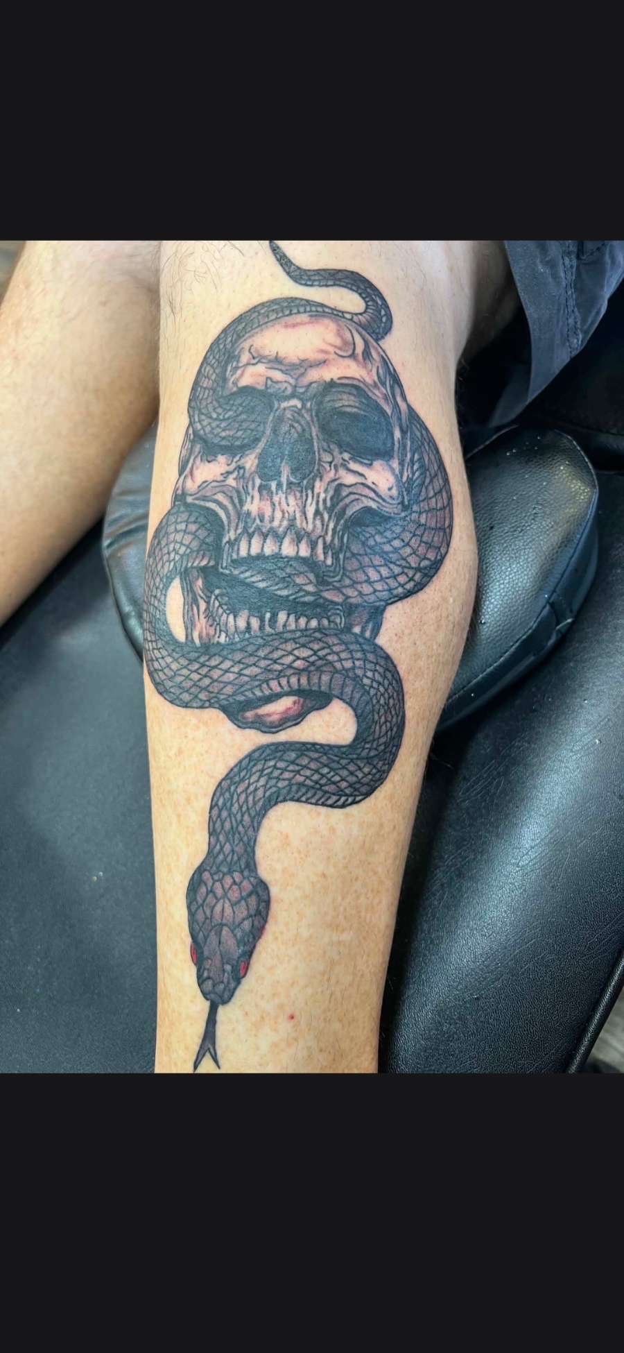 Black and grey skull wrapped by a snake calf tattoo