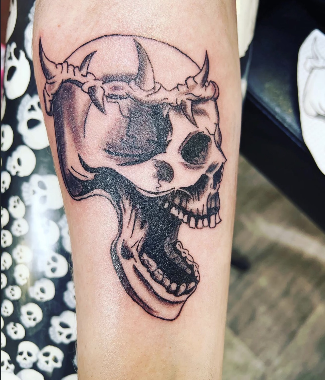 Black and grey skull wearing a horned fang crown forearm tattoo